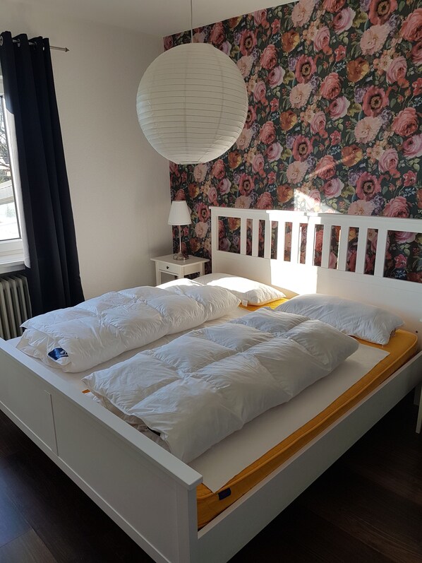 A bed with white bedding, a floral wallpaper, and a hanging light fixture.