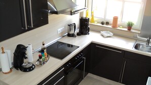 A modern kitchen with black cabinets, a stainless steel range hood, a built-in oven, a dishwasher, and a window with potted plants. - Holiday house in Duhnen with a large garden and lots of space (Cuxhaven)