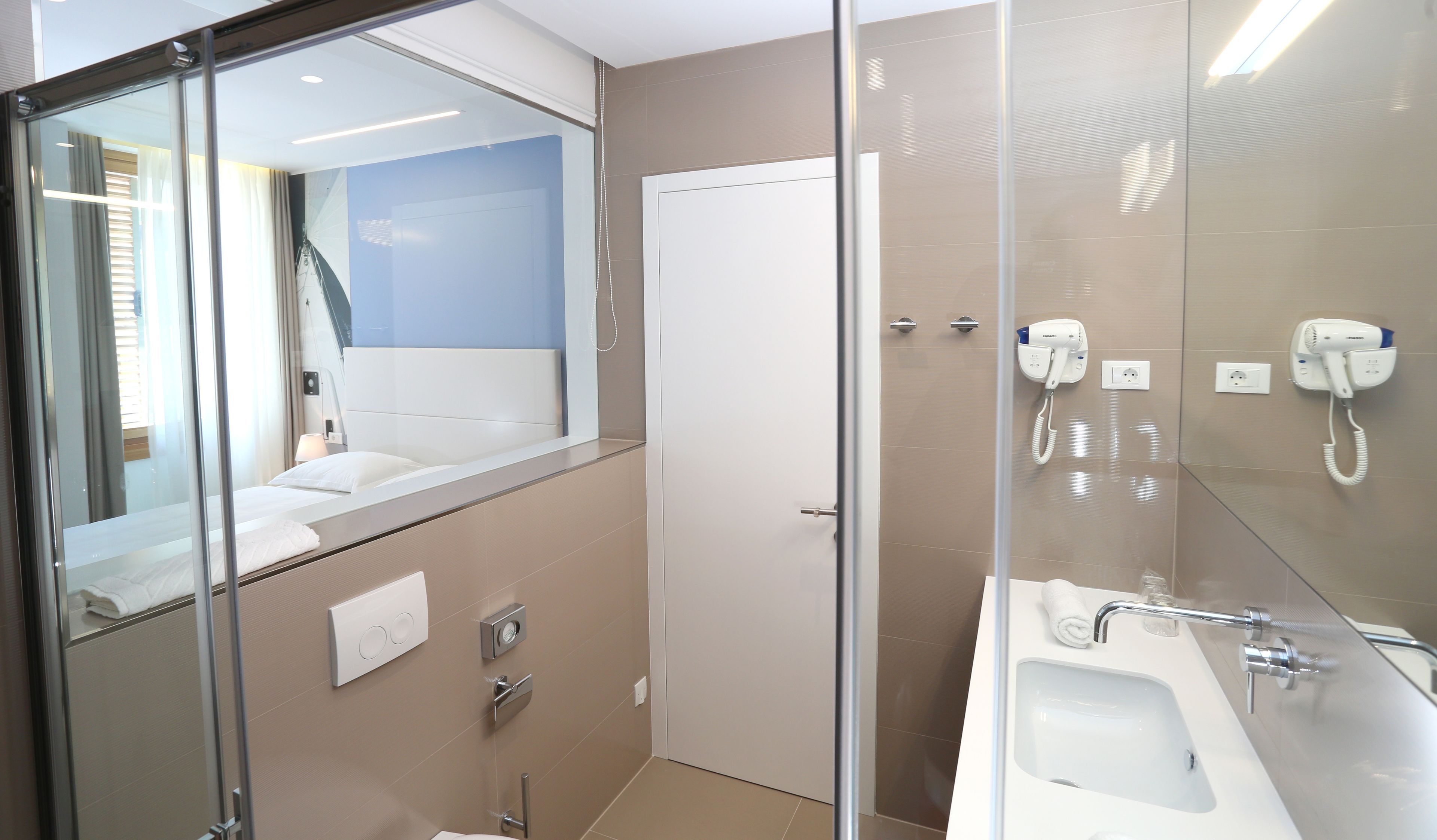 A modern bathroom with a glass shower enclosure, a white sink, and a hairdryer mounted on the wall.