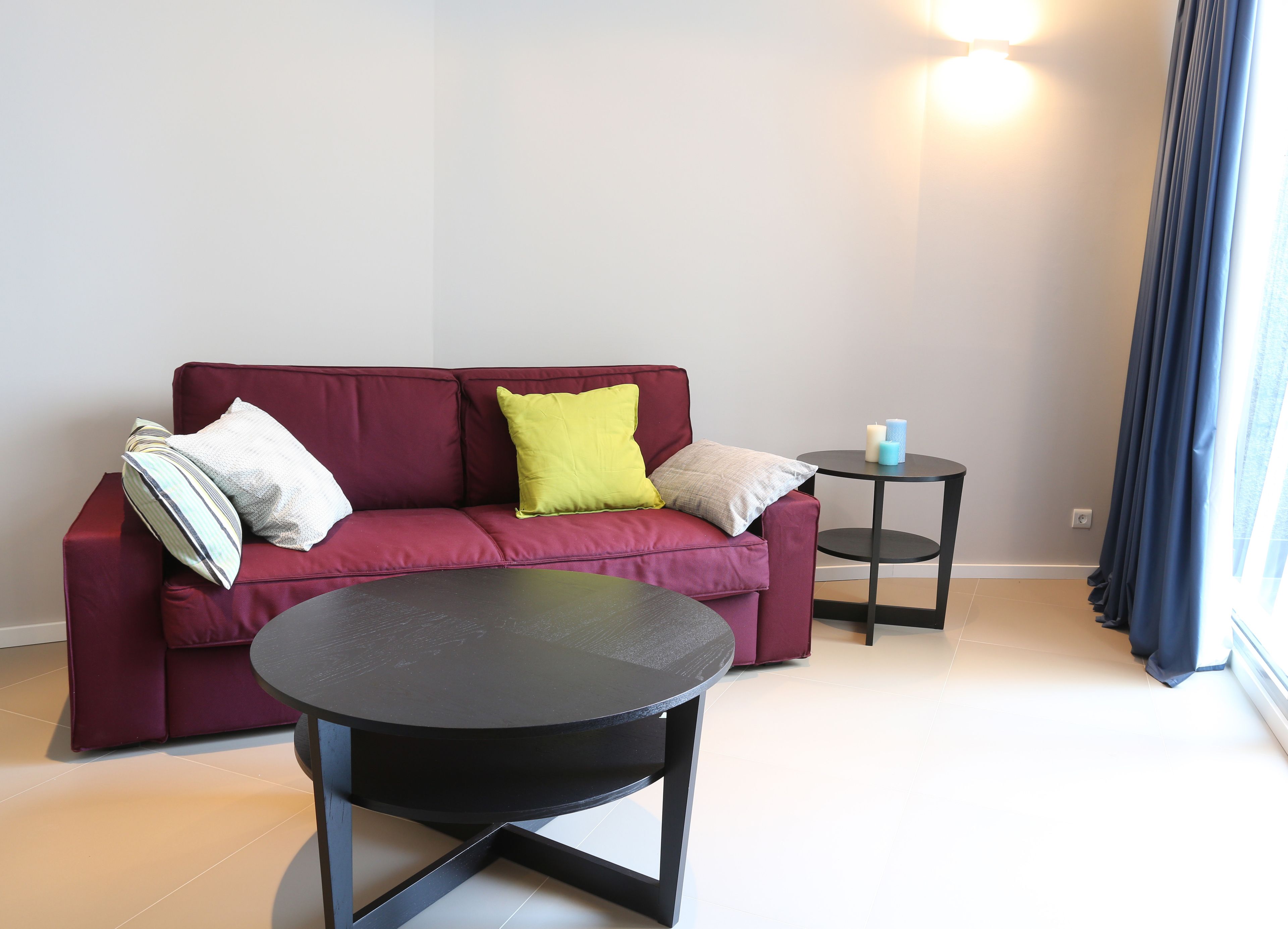 A modern living room with a red sofa, a round black coffee table, and a small side table with candles.
