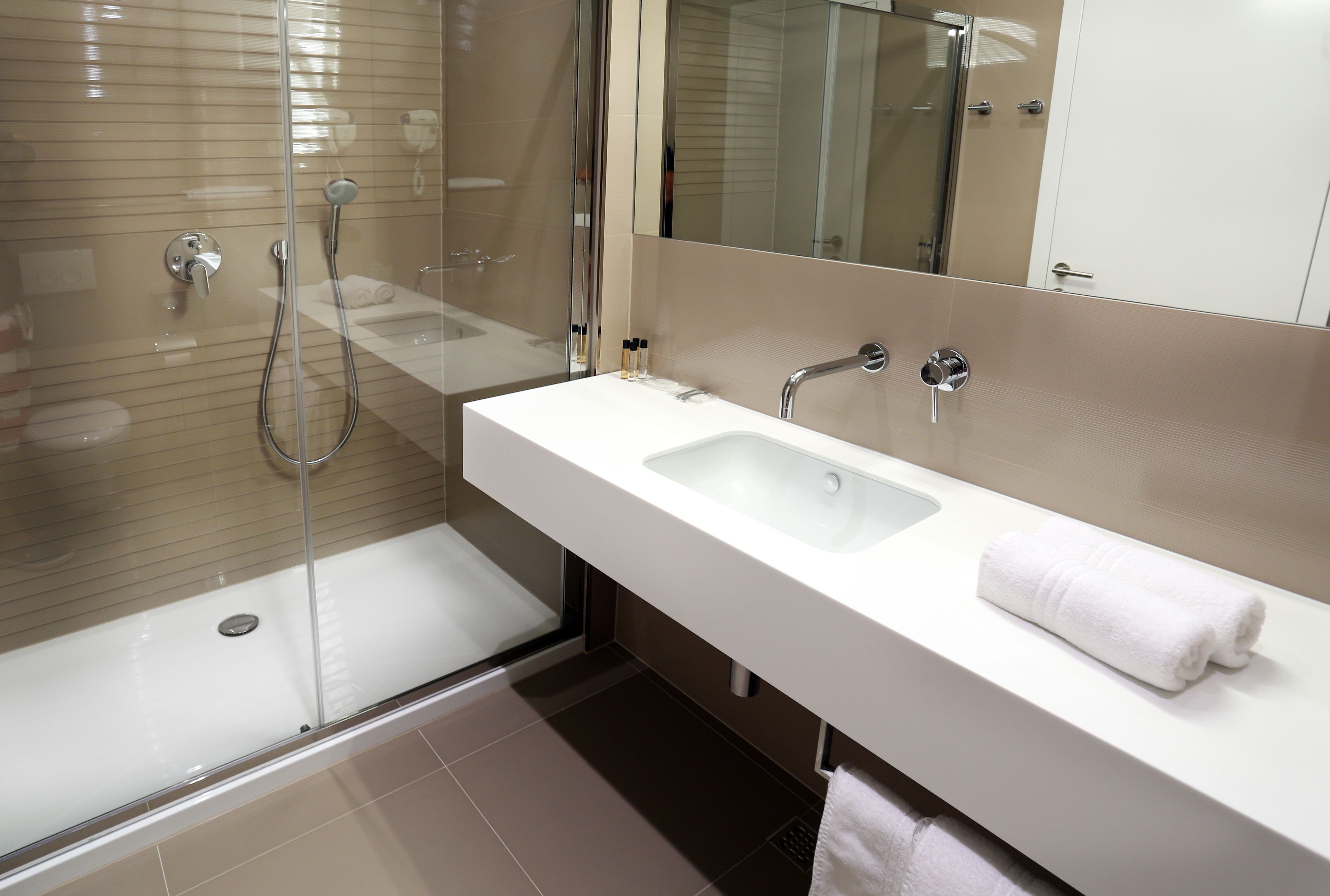 A modern bathroom with a glass-enclosed shower, a white sink, and a large mirror.