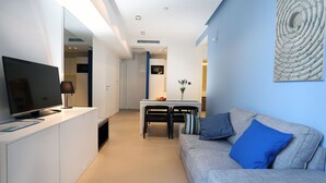 A modern living room with a flat-screen TV, a dining table with chairs, and a sofa with blue cushions. - Guesthouse Villa Scalaria (Split)
