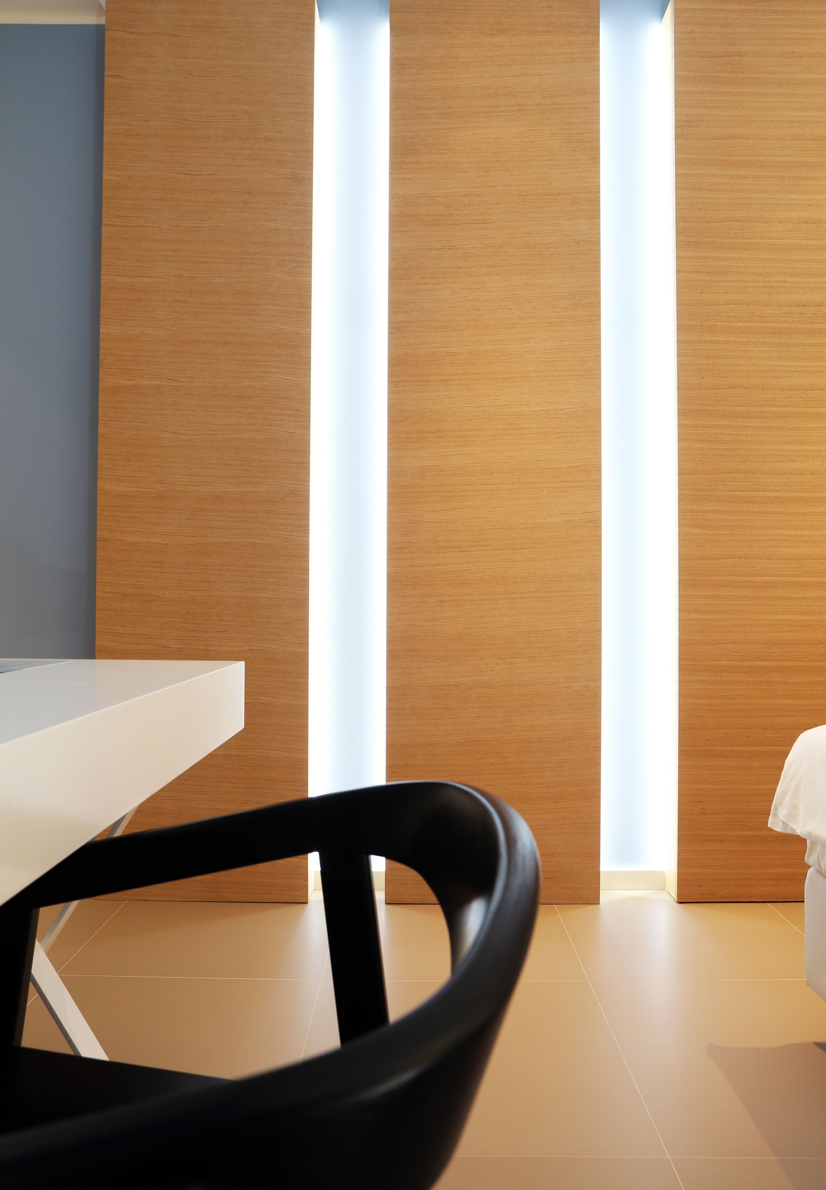 Une chambre d’hôtel moderne avec un mur d’accent en bois, une table de chevet blanche et une chaise noire.