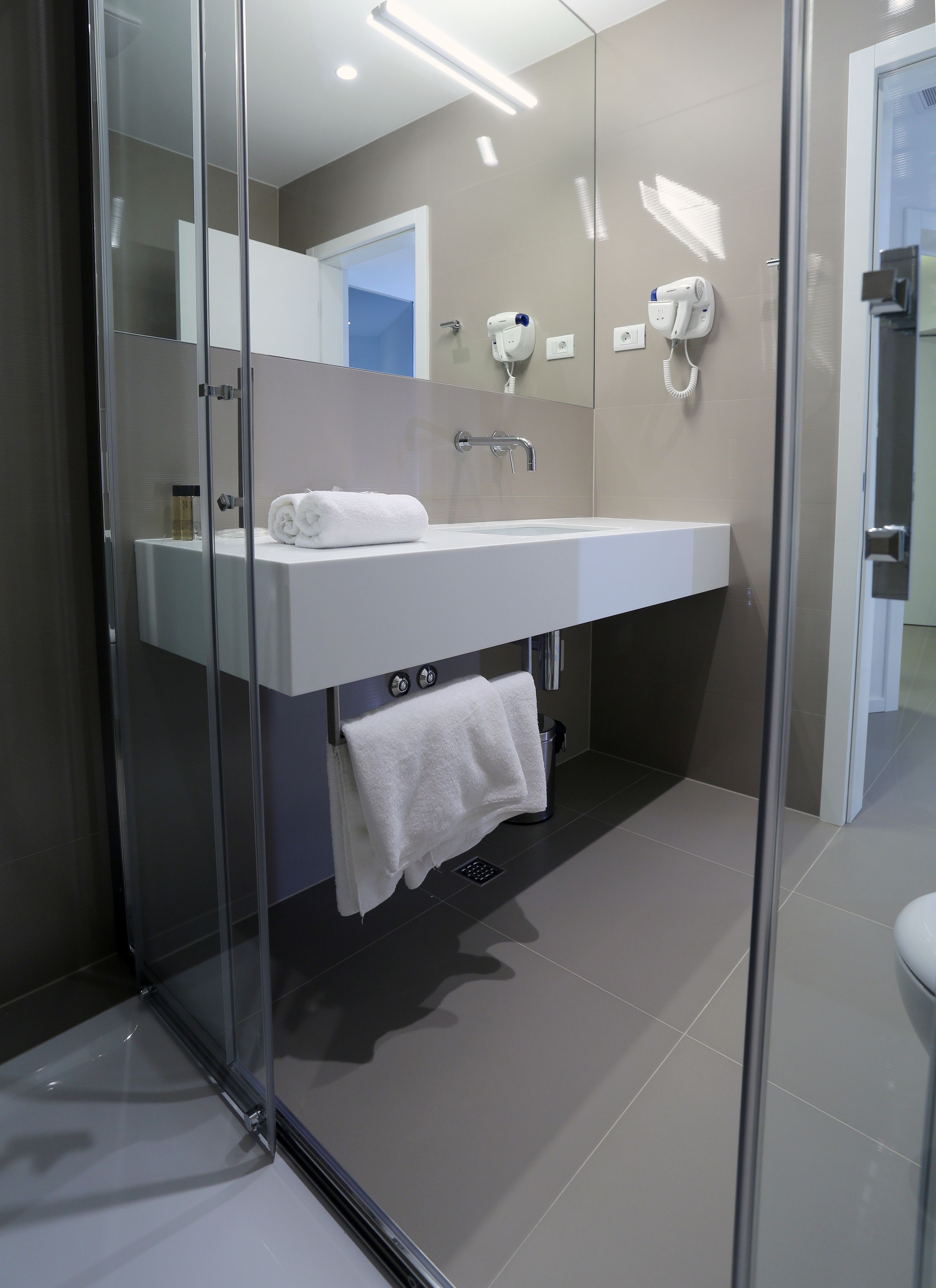 Een moderne badkamer met een douchecabine van glas, een wit wastafelmeubel en een handdoekrek.