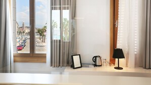A hotel room with a large window, curtains, a bedside table with a lamp, a picture frame, and a kettle. - Guesthouse Villa Scalaria (Split)