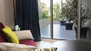 A modern living room with a sofa, a small table, and a view of a balcony with potted plants. - Guesthouse Villa Scalaria (Split)