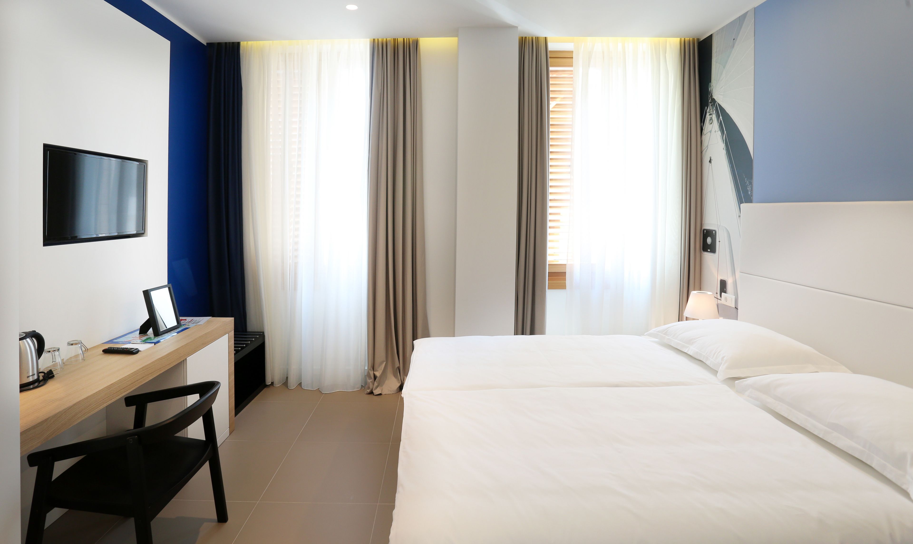 A hotel room with a bed, a desk with a chair, a television, and curtains.