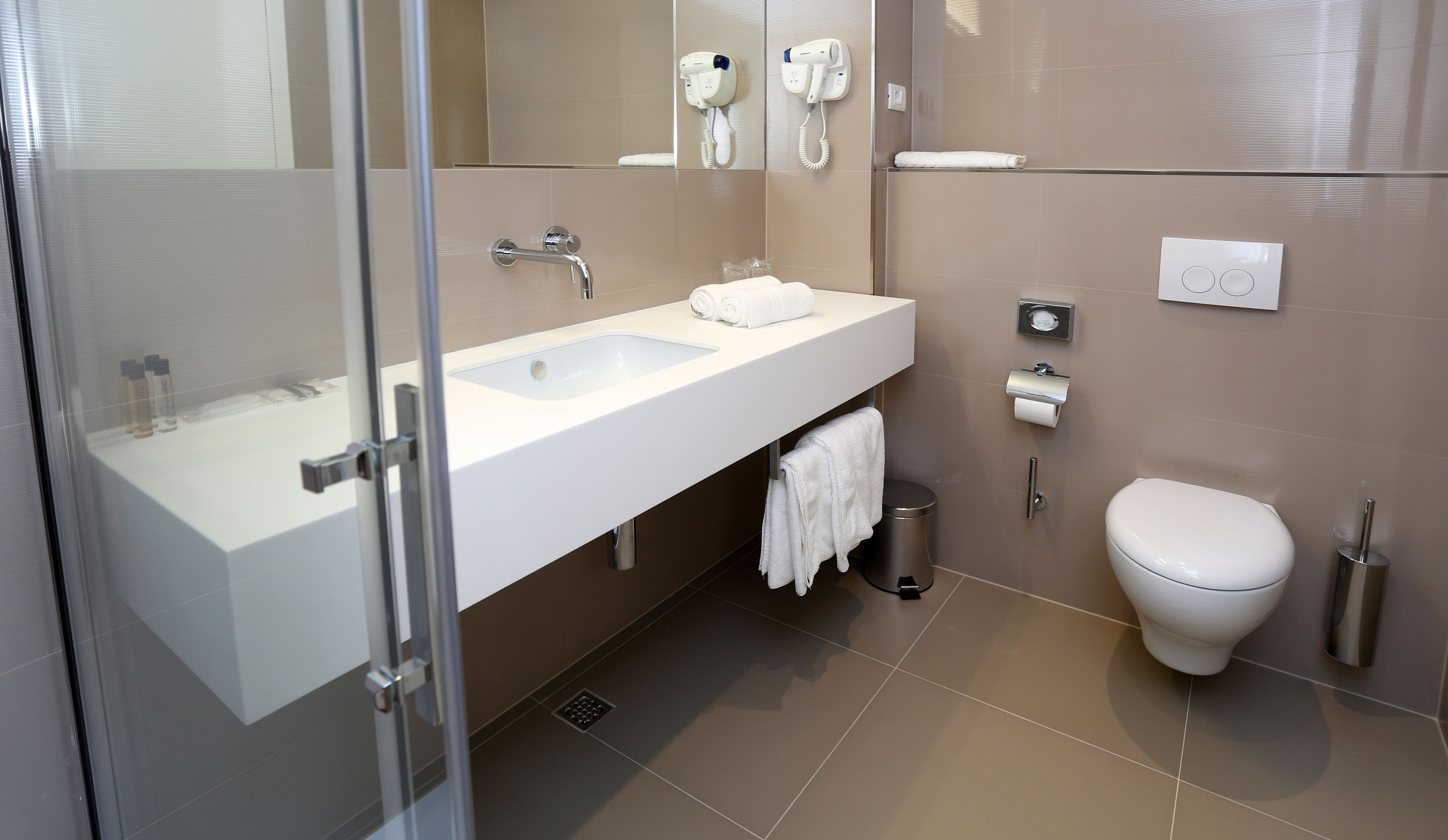 Une salle de bain moderne avec une douche à parois de verre, un lavabo blanc, des toilettes et un sèche-cheveux fixé au mur.