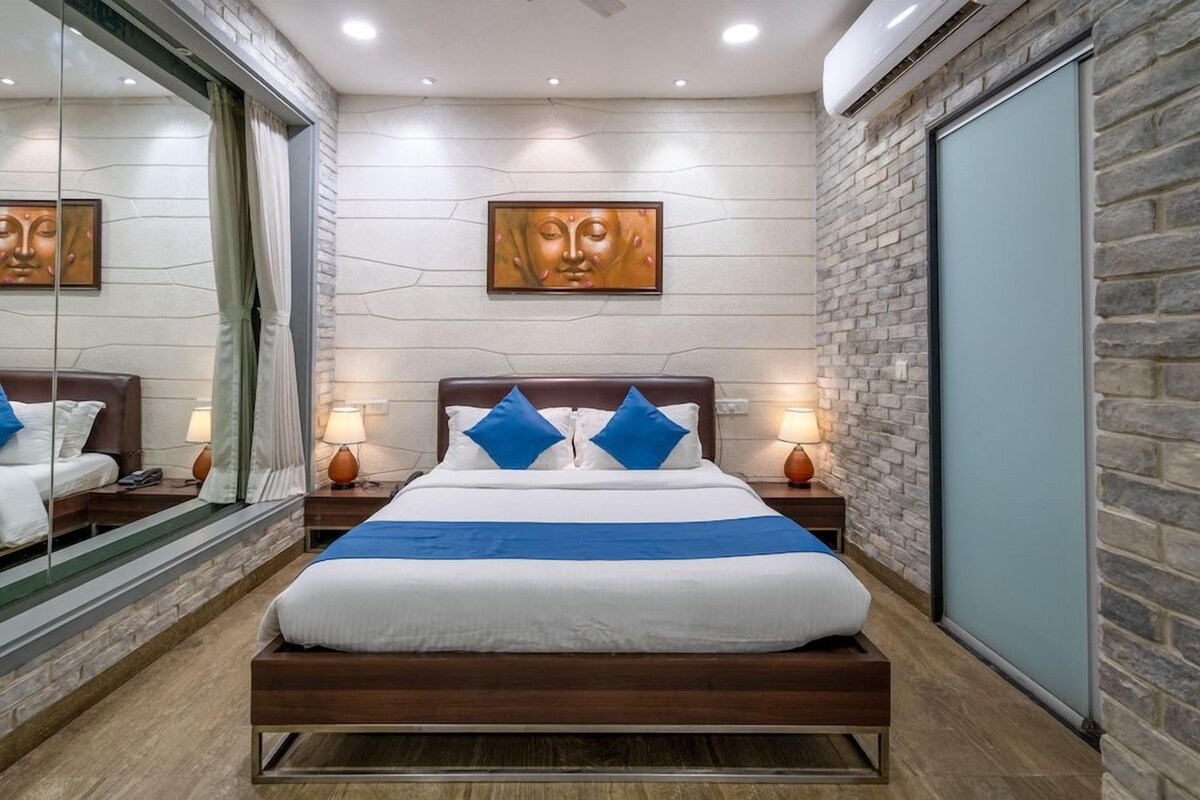 A modern hotel room with a large bed, two bedside tables with lamps, a large mirror, and a wall-mounted artwork.