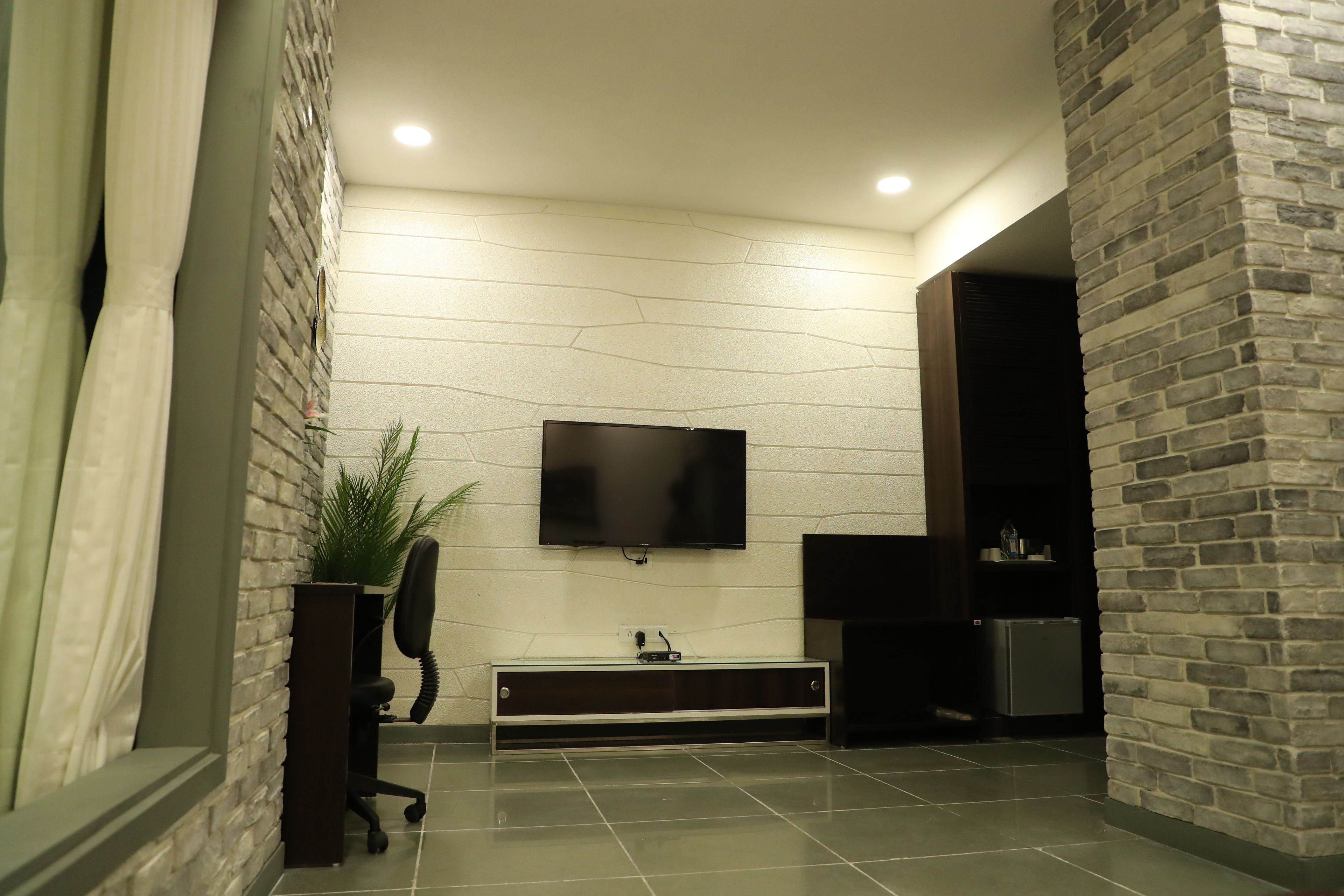 A modern interior with a flat-screen TV mounted on a white wall, a dark wooden bench with a glass top, and a potted plant.