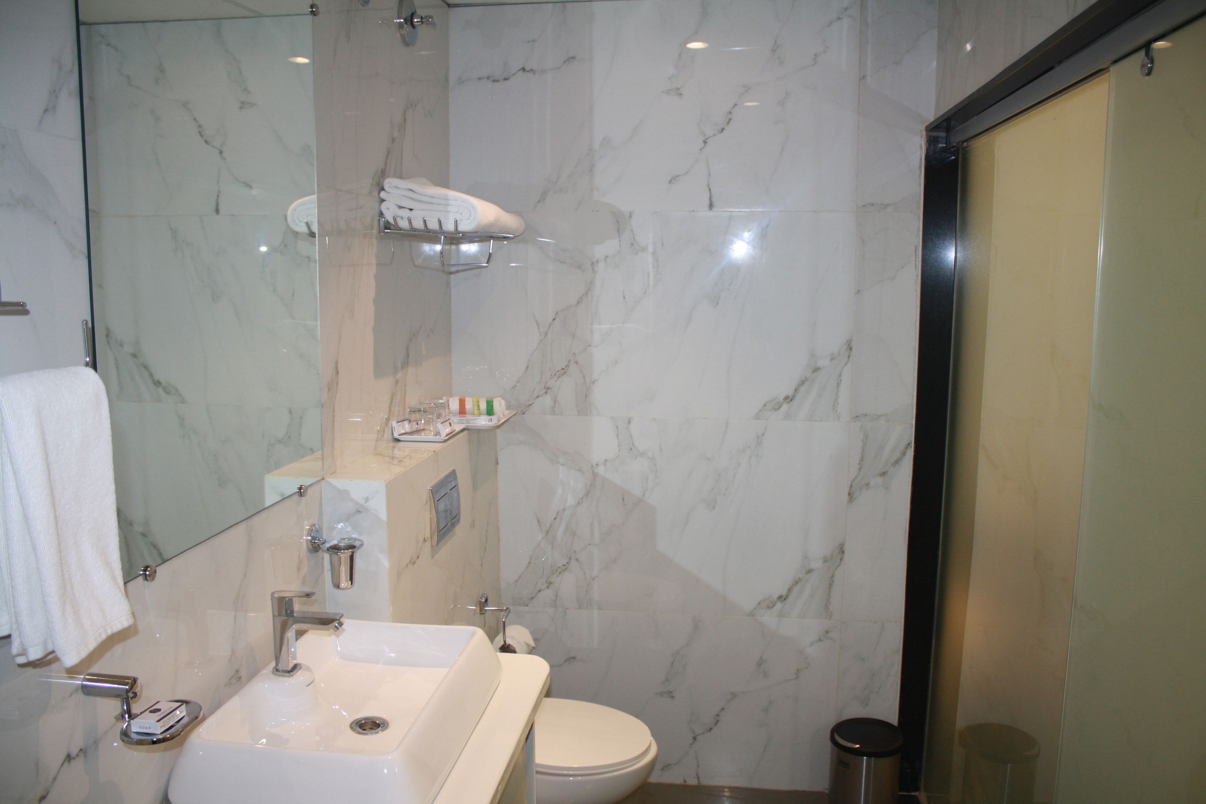 Een badkamer met een marmeren wastafel, toilet en een douche met glazen wanden.