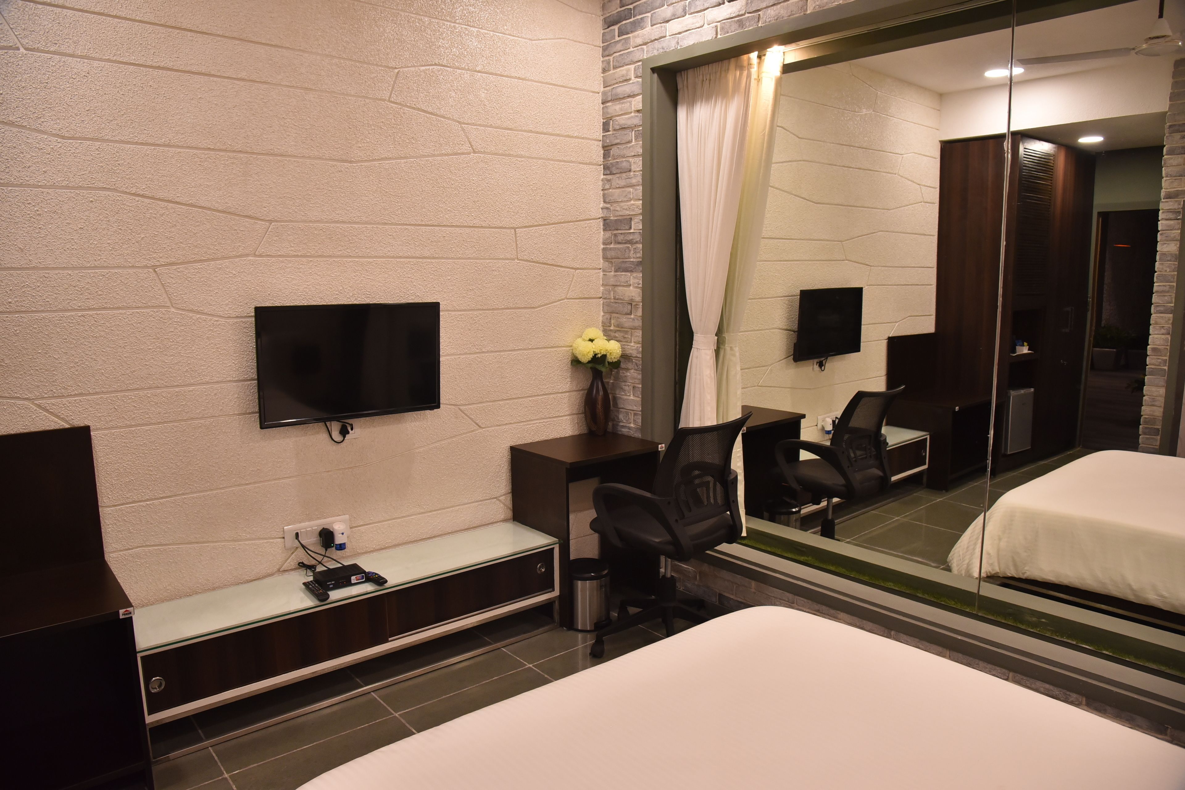 Habitación de hotel con cama, escritorio con silla, televisor y espejo que refleja la habitación.