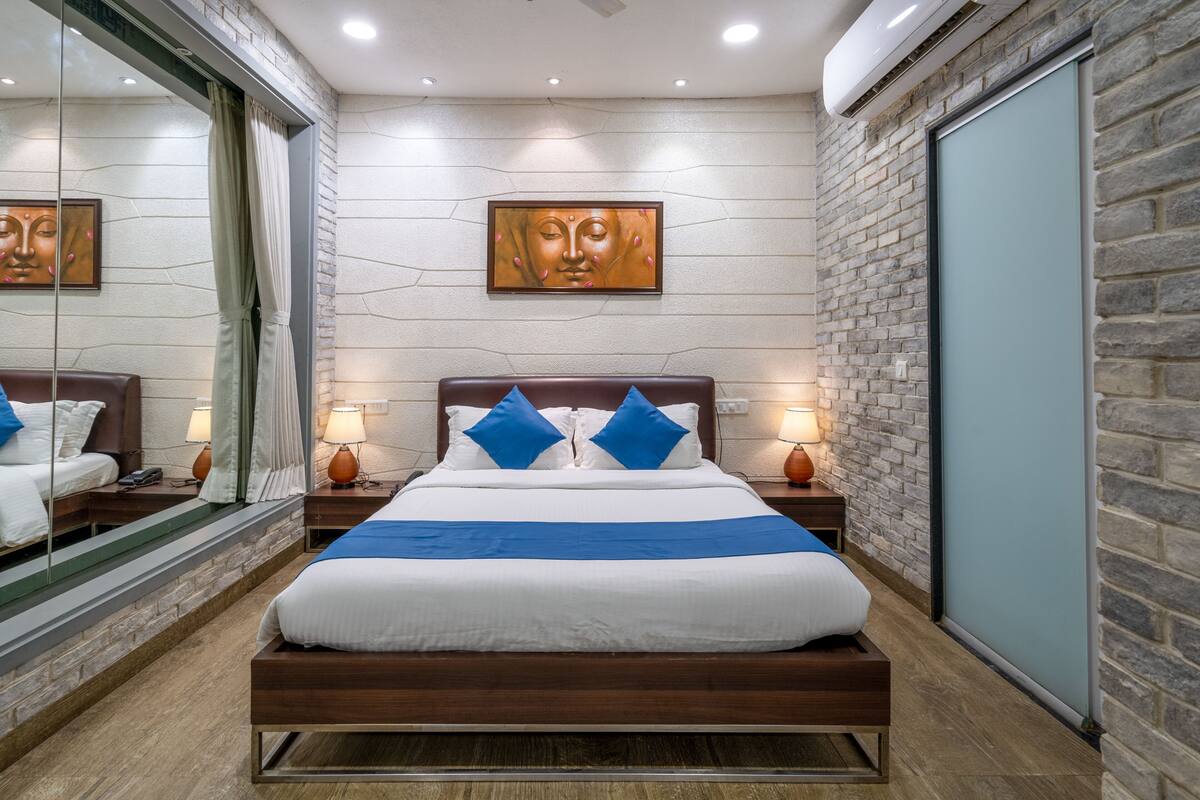 A modern hotel room with a large bed, two bedside tables with lamps, a large mirror, and a stone wall.