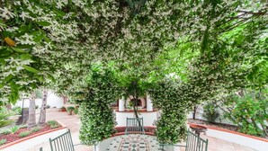 Un espacio al aire libre cubierto, con suelo estampado, rodeado de follaje y un edificio blanco al fondo.