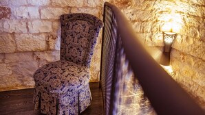 Una silla con estampado floral en una habitación con paredes de piedra y una lámpara de pared encendida.