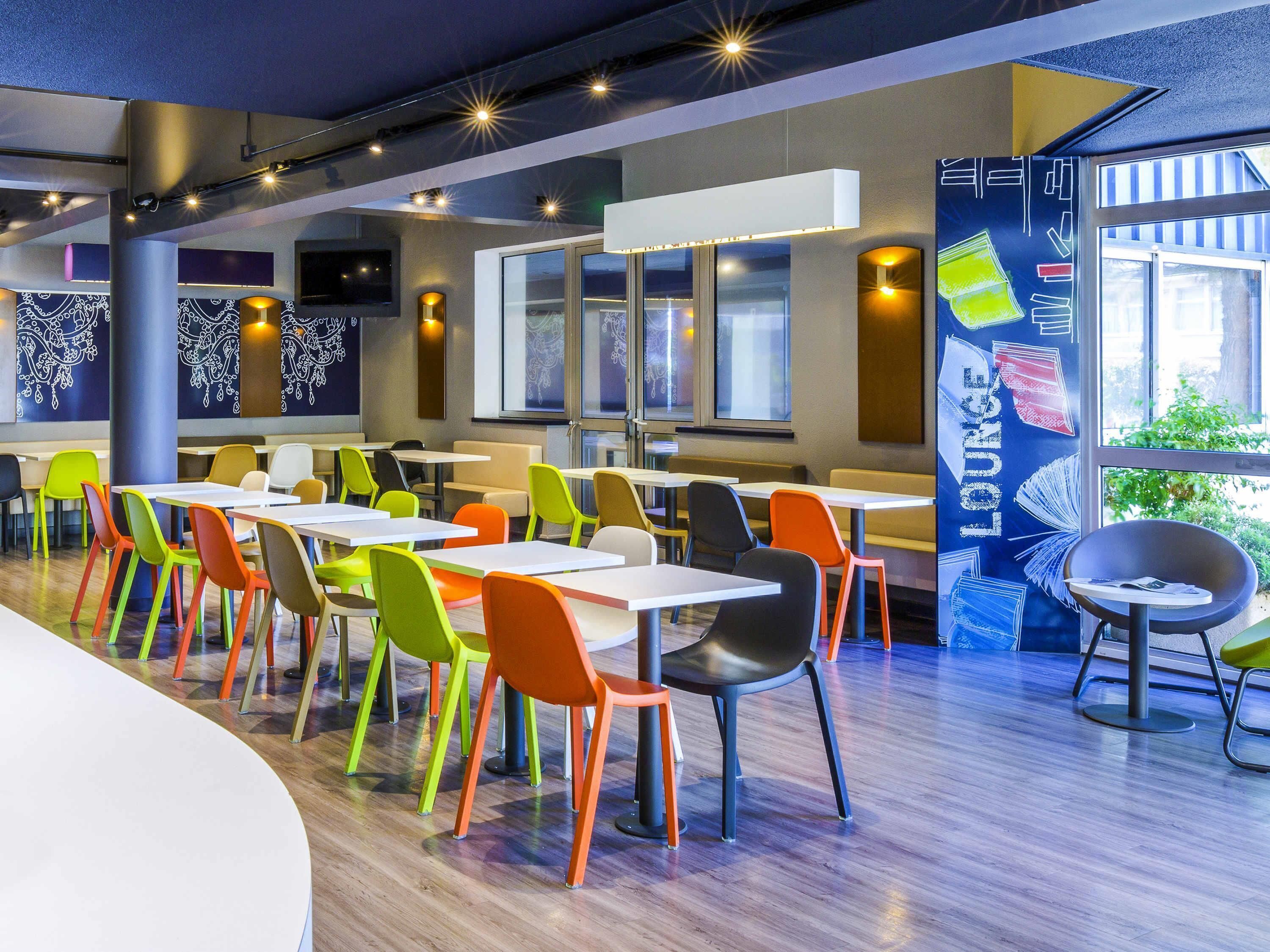 Un comedor moderno con sillas y mesas coloridas, ventanas amplias y vistas al exterior.