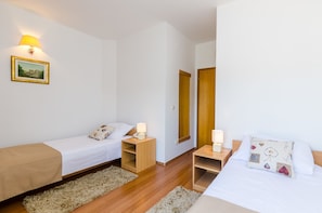 Une chambre d’hôtel avec deux lits simples, des tables de chevet en bois, un miroir et un petit tapis.