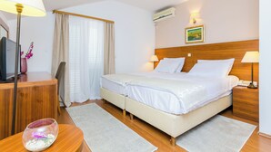 Une chambre d’hôtel avec deux lits, une tête de lit en bois, un bureau avec une lampe, une télévision et une fenêtre avec des rideaux.