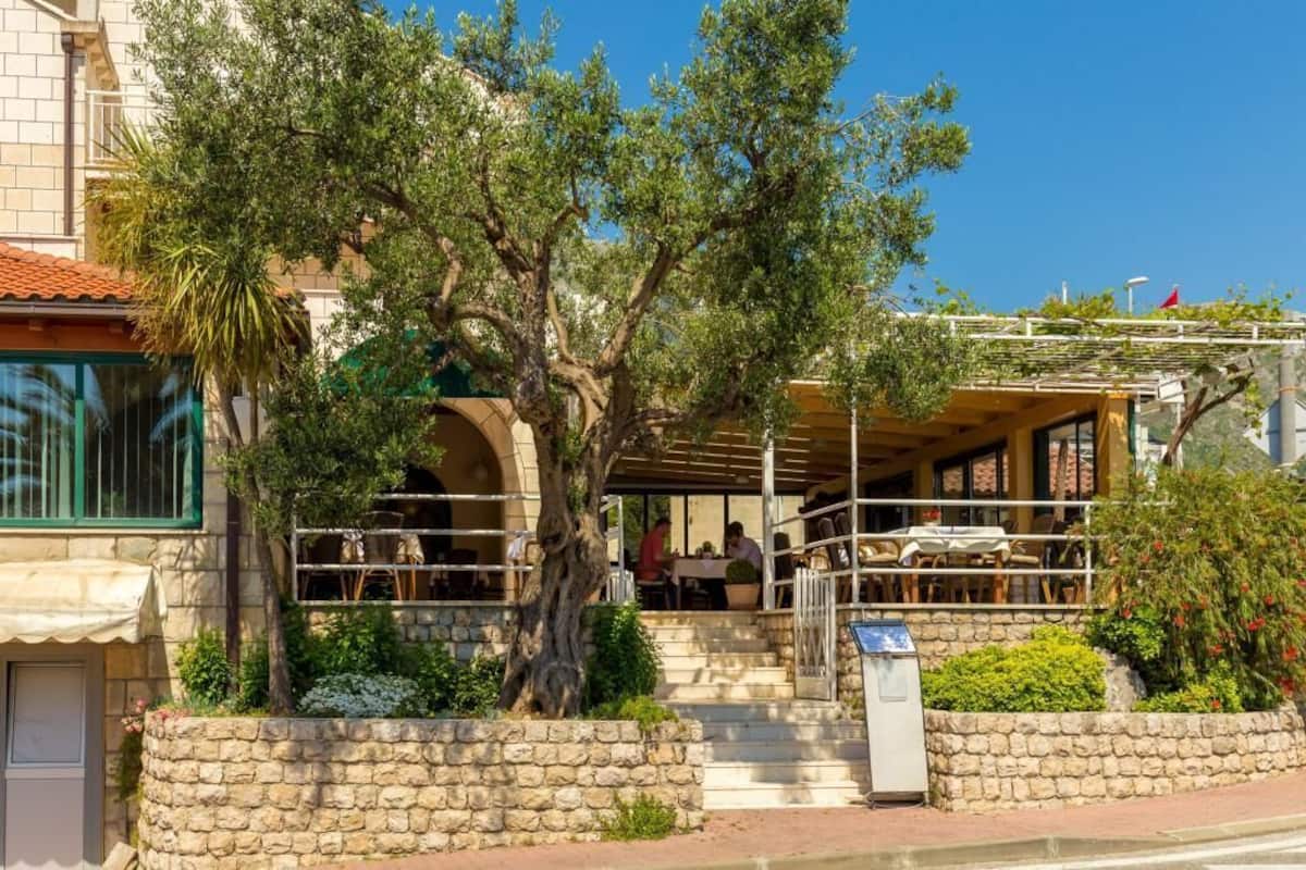 A restaurant with outdoor seating, stone walls, and a tree in the center.