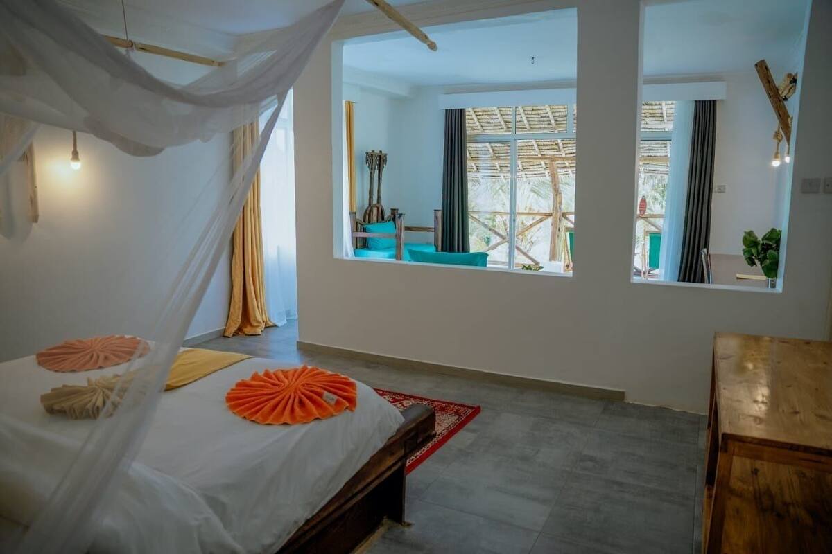 A room with a bed, a window, a wooden table, and a view of the outside.