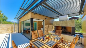 An outdoor patio with a wooden table, chairs, and a grill area. - Cozy apartment in Kastel Stari (Kastel Stari)