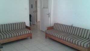 Una sala de estar con dos sofás a rayas, piso de baldosas y una puerta que da a otra habitación.