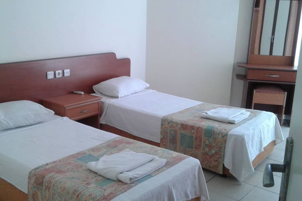 Une chambre d’hôtel avec deux lits, chacun recouvert d’une courtepointe blanche et d’une couverture à motifs. On y trouve une table de chevet en bois avec un téléphone et une prise électrique murale.