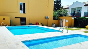 A rectangular swimming pool with a tiled deck, surrounded by a yellow building with a window and a door. - Hostal Miramar (Barbate)