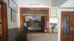 A reception desk with a wooden frame, a clock, and a plant. - Hostal Miramar (Barbate)