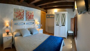 Un dormitorio con cama, mesitas de noche, radiador, armario y cuadros en la pared.