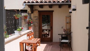 Un pequeño patio al aire libre con mesa y sillas de madera, plantas en macetas y techo de baldosas.
