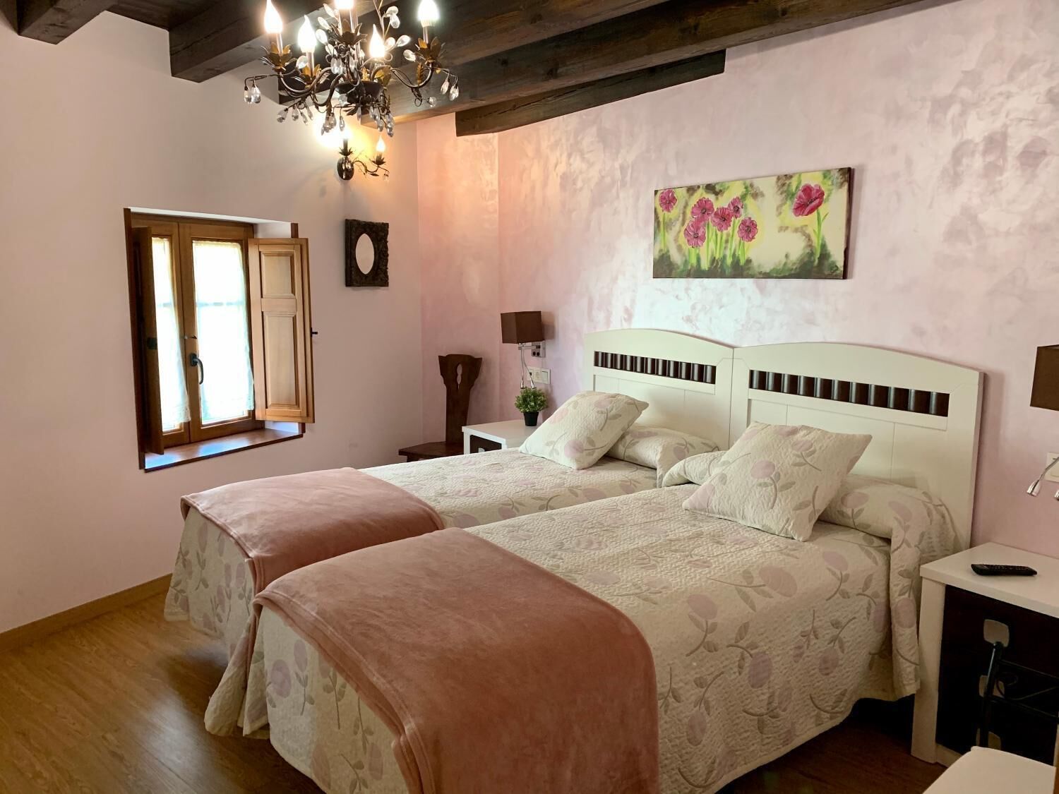 Un dormitorio con dos camas, una araña, un cuadro y una ventana con cortinas.