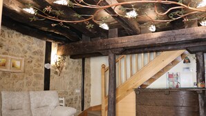 Un interior rústico con pared de piedra, vigas de madera, una escalera de madera y un sofá.