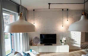 Ein modernes Wohnzimmer mit weißer Ziegelwand, Flachbildfernseher und Pendelleuchten.