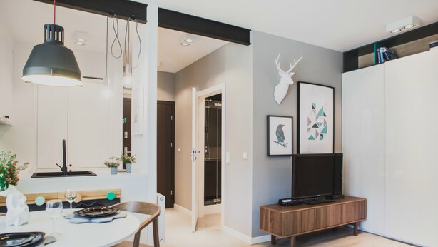 A modern kitchen with a dining area, a TV on a wooden stand, and a wall-mounted deer head decoration. - Apartamenty Gdańsk-Old Town Szafarnia 6a (Gdansk)
