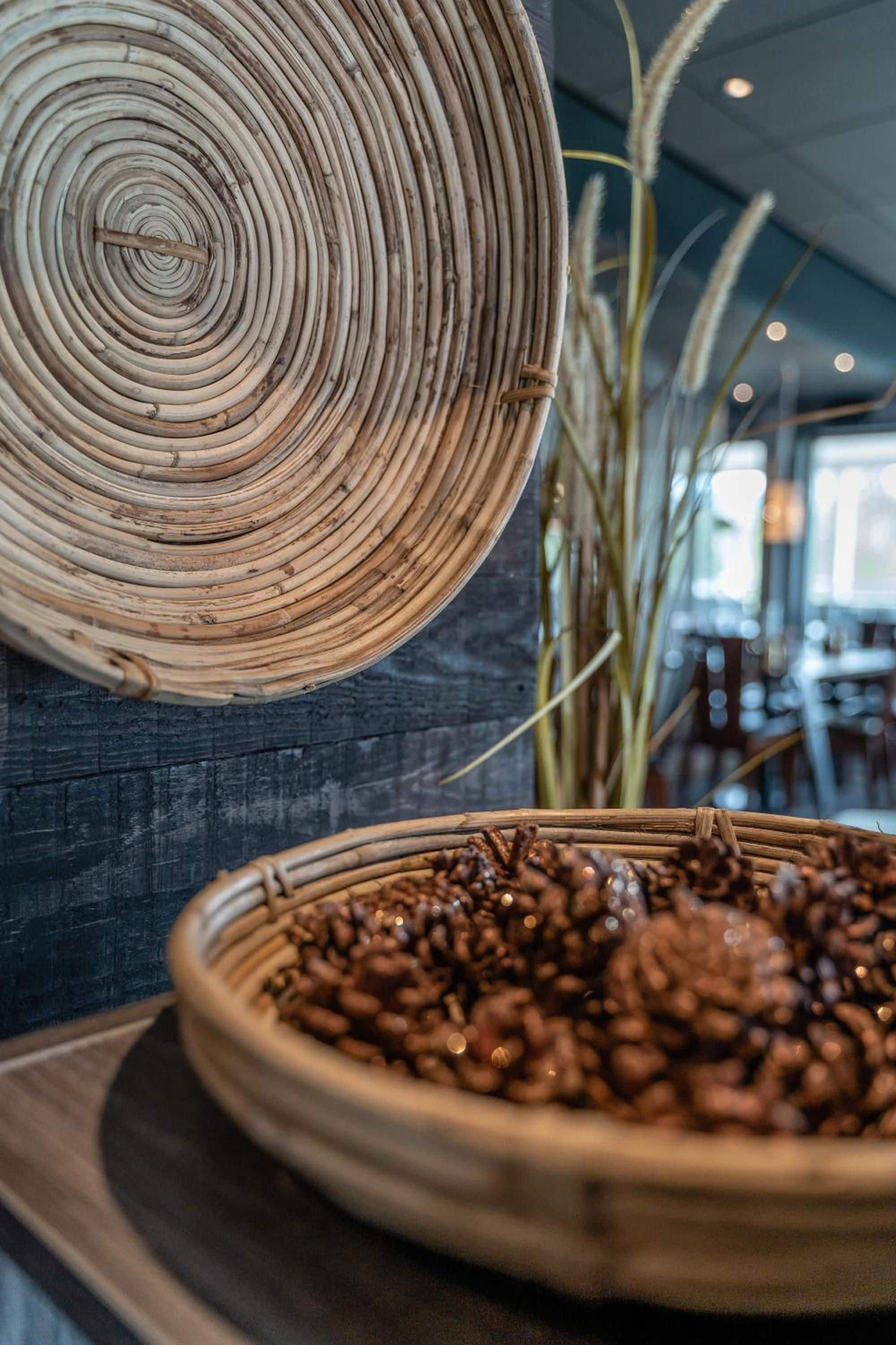 A woven basket filled with coffee beans on a table, with a woven mat hanging on the wall behind it.