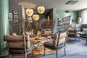 A modern lounge area with wicker chairs, a round coffee table, and pendant lighting. - Storforsen Hotell (Vidsel)