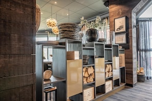 Un intérieur moderne avec des étagères en bois où sont exposés divers objets, un luminaire suspendu et une fenêtre avec des rideaux.