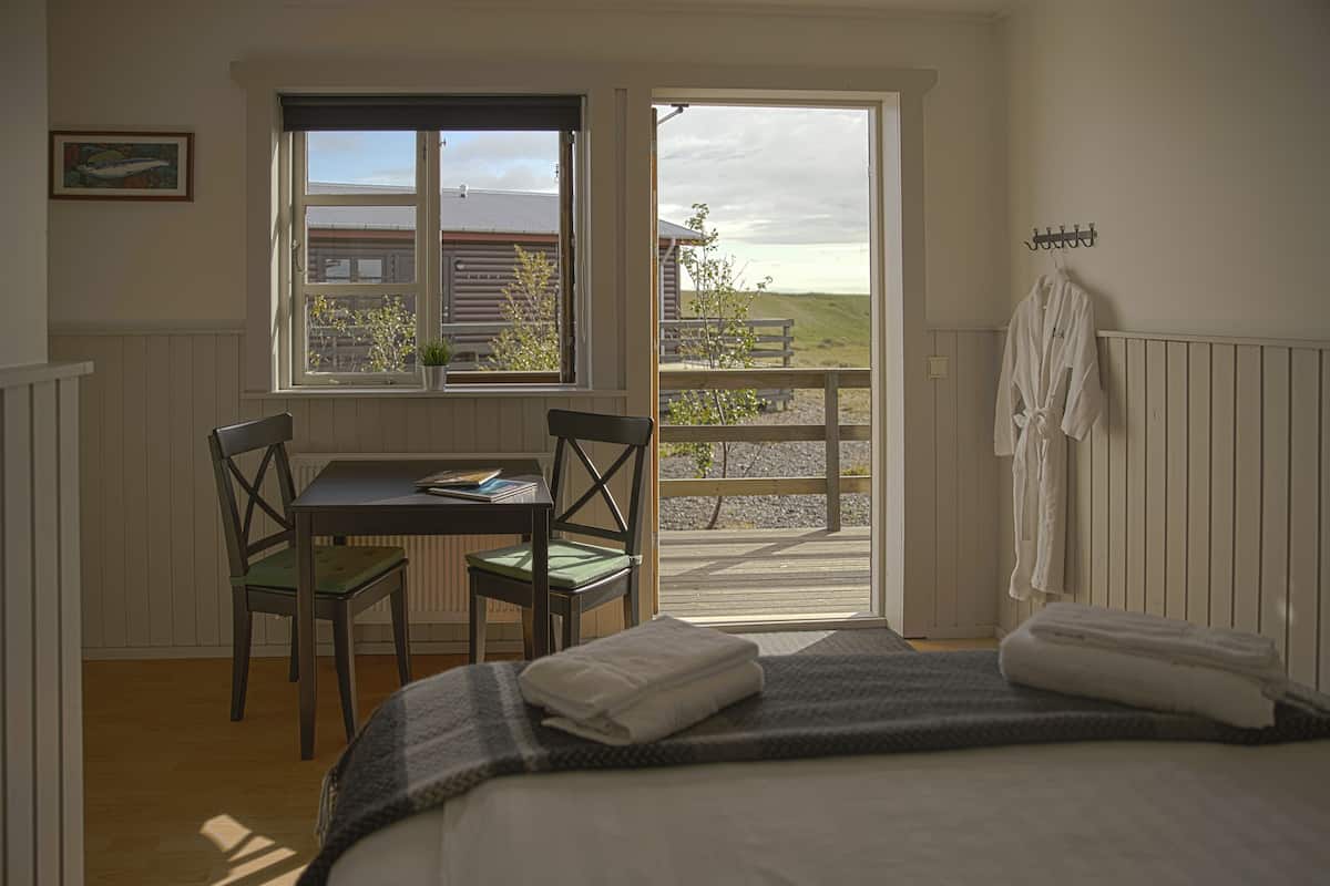 A bedroom with a bed, a window, a table with chairs, and a view of a grassy area.