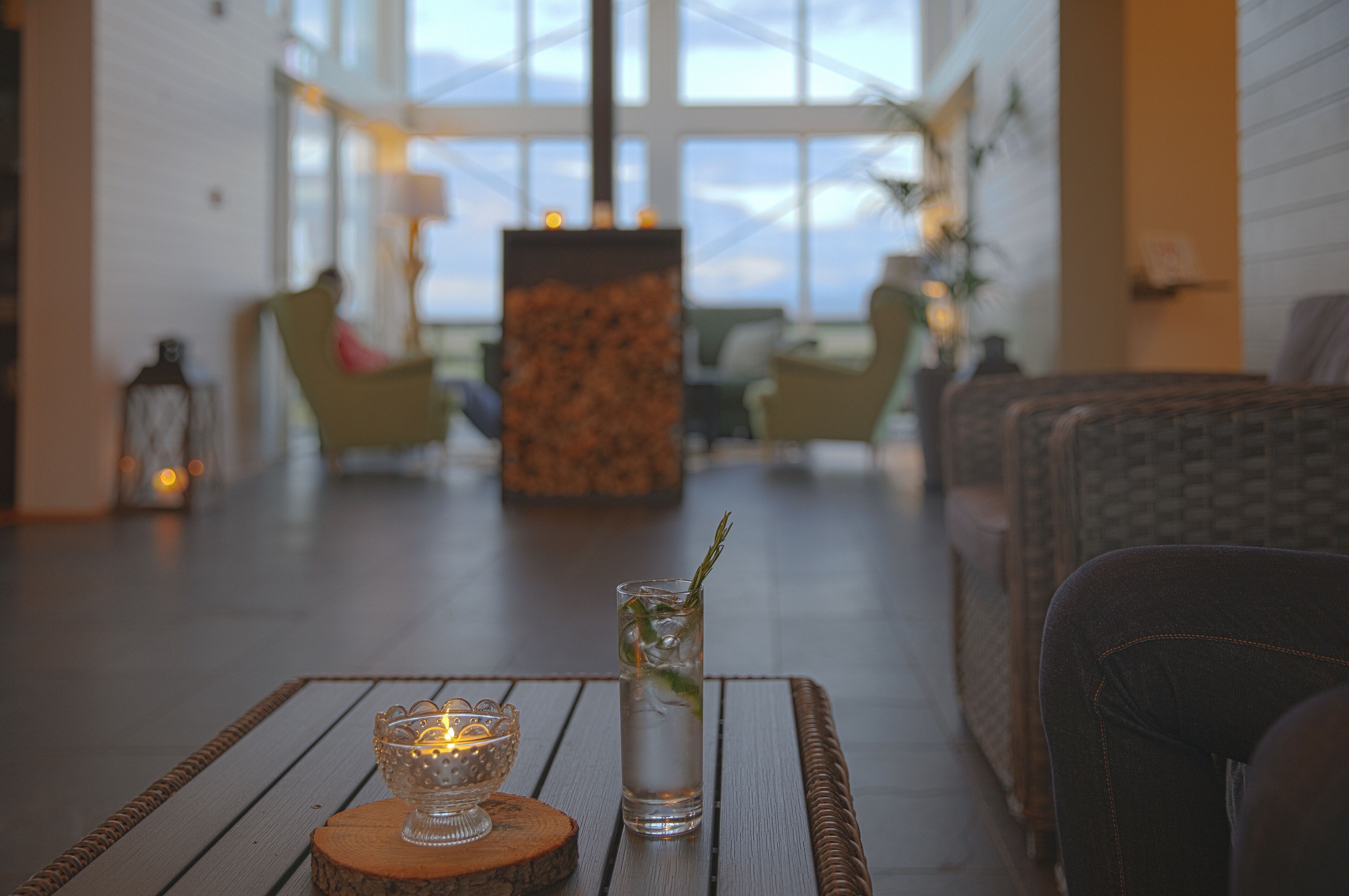 Un ambiente interior acogedor con una mesa de madera, un vaso de agua con una ramita de romero y una vela encendida.