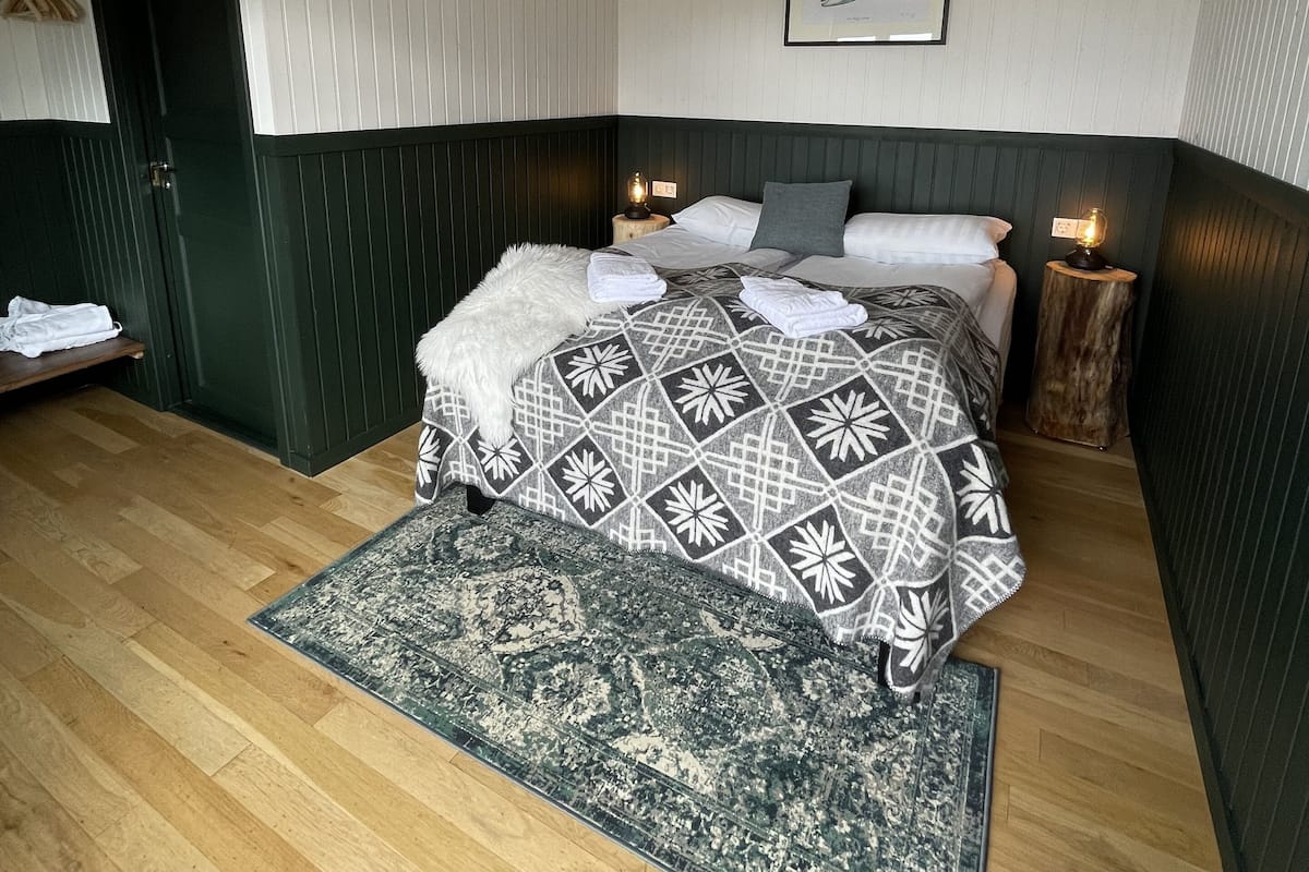 A bedroom with a bed, a rug, a wooden floor, a door, and a wall-mounted picture.