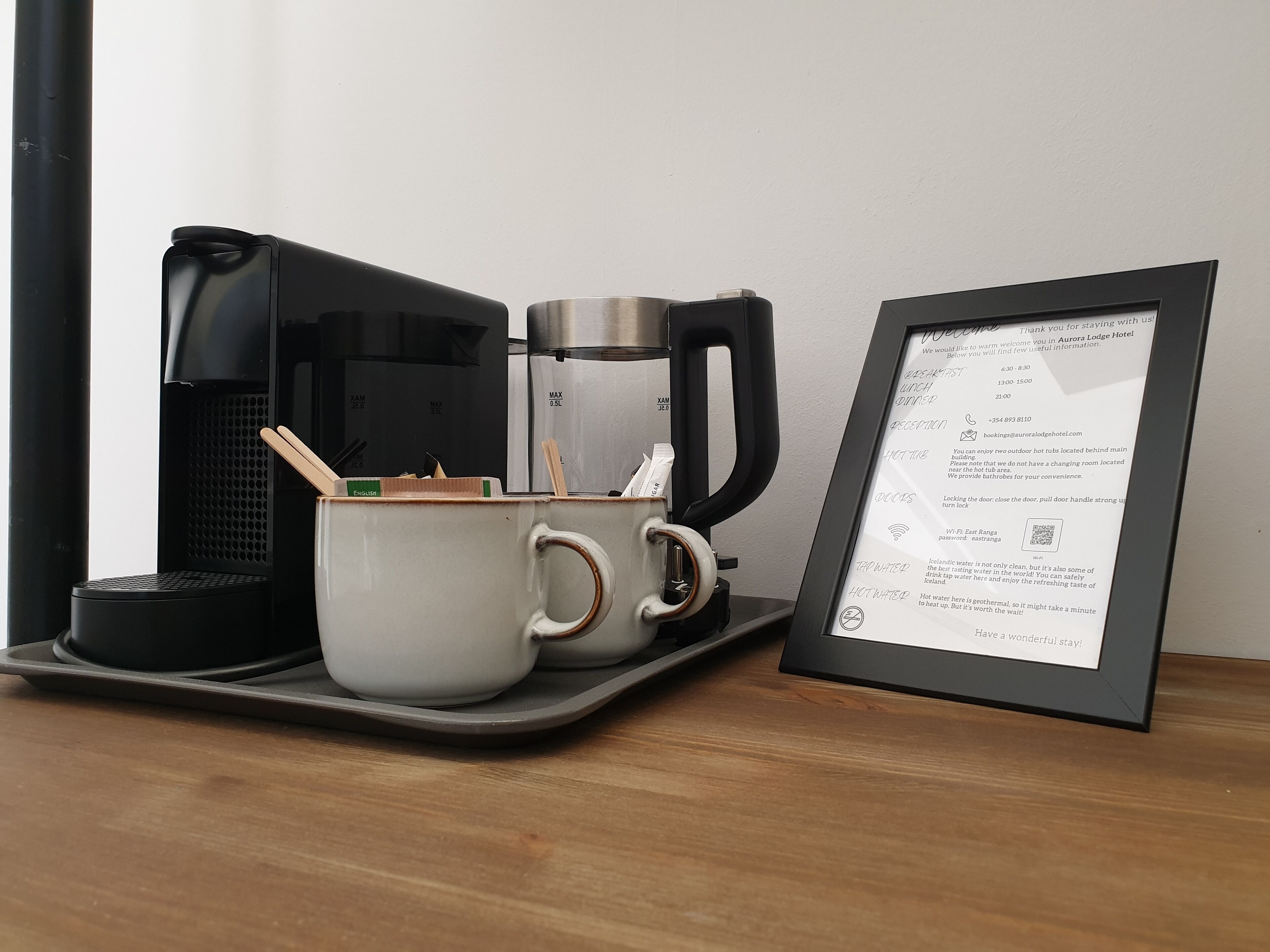 Uma cafeteira, duas chávenas e um letreiro de boas-vindas emoldurado sobre um tabuleiro.