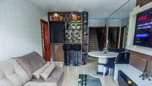 A modern living room with a beige sofa, a round dining table, and a bar area with various bottles. - Charme Apartamento Centro de Gramado (Gramado)