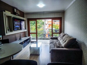 Una sala moderna con un sofá, un televisor montado en la pared y un balcón con vistas a edificios.