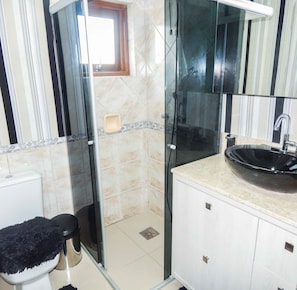 Een badkamer met een douchecabine van glas, toilet en een wastafel met spiegel erboven.