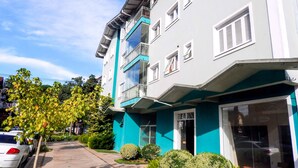 A multi-story building with balconies, a tiled sidewalk, and greenery. - Charme Apartamento Centro de Gramado (Gramado)