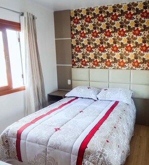 Een slaapkamer met een bed, een hoofdeinde, een raam met gordijnen en een wand met bloemenmotief.