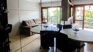 A modern living room with a sofa, a dining table with chairs, and a balcony with a railing. - Charme Apartamento Centro de Gramado (Gramado)