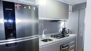 A modern kitchen with a stainless steel refrigerator, a gas stove, and grey cabinetry. - Charme Apartamento Centro de Gramado (Gramado)