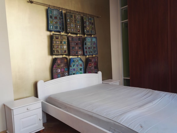 A bedroom with a white bed, a nightstand, and a wall-mounted quilt rack with colorful quilts.